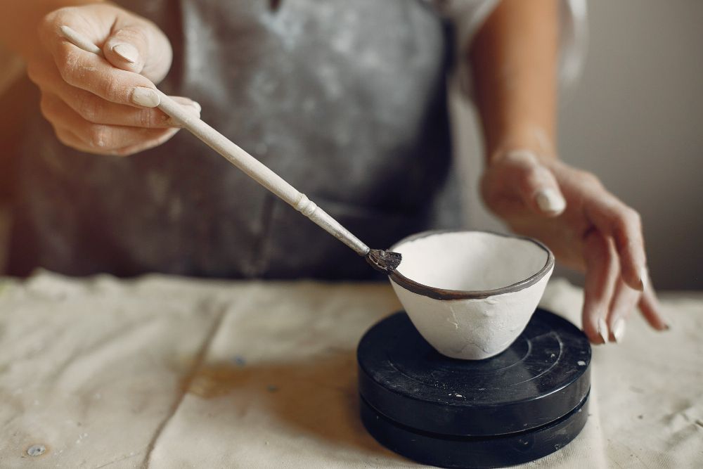 Dłonie szkliwią ceramiczną miskę pędzlem